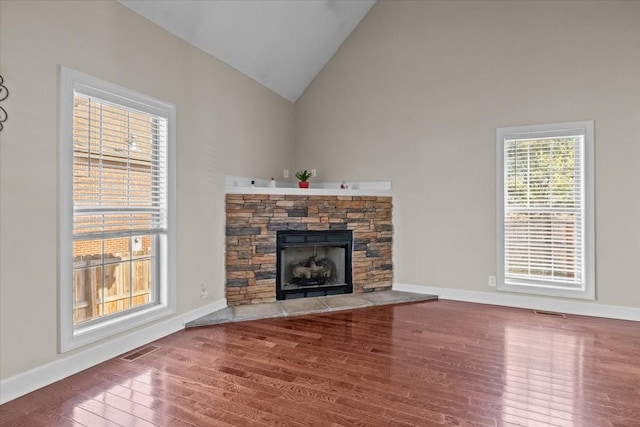 unfurnished living room with hardwood / wood-style flooring, a stone fireplace, and high vaulted ceiling