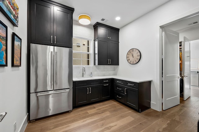 kitchen with stainless steel fridge, light hardwood / wood-style floors, sink, and backsplash