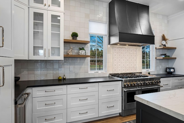 kitchen featuring backsplash, premium range hood, white cabinets, and range with two ovens