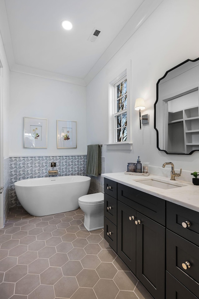 bathroom featuring tile walls, ornamental molding, tile patterned floors, a tub, and toilet