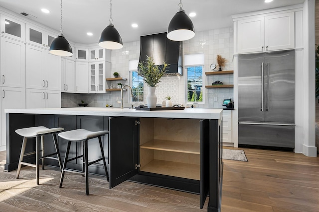 kitchen featuring white cabinetry, decorative backsplash, stainless steel built in fridge, and a center island with sink