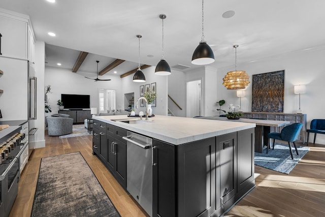 kitchen with hardwood / wood-style floors, pendant lighting, beamed ceiling, an island with sink, and sink