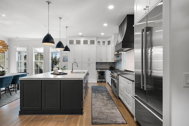 kitchen with sink, wine cooler, high end appliances, a kitchen island with sink, and custom range hood