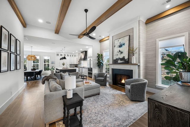 living room with ceiling fan, dark wood-type flooring, a large fireplace, and beamed ceiling