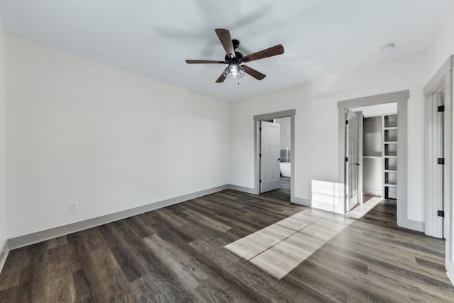 unfurnished bedroom featuring ceiling fan, a spacious closet, a closet, and dark wood-type flooring