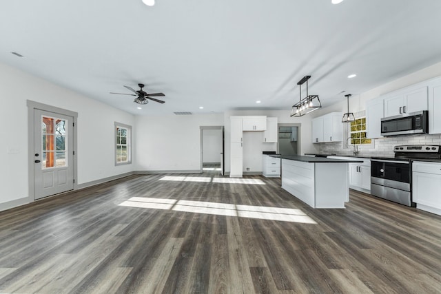 kitchen with appliances with stainless steel finishes, white cabinets, a kitchen island, and decorative light fixtures