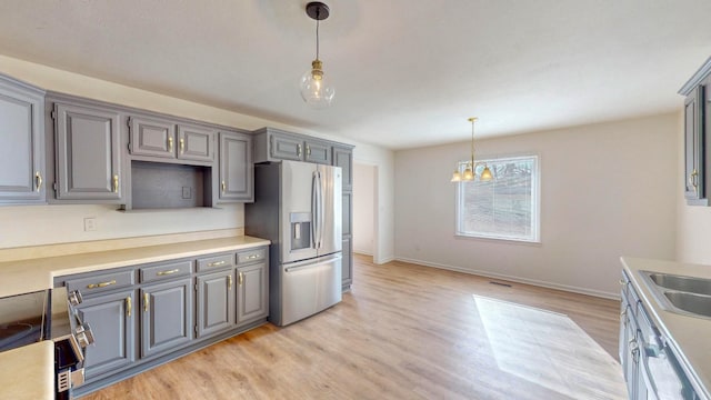 kitchen featuring pendant lighting, stainless steel appliances, light hardwood / wood-style floors, sink, and a chandelier