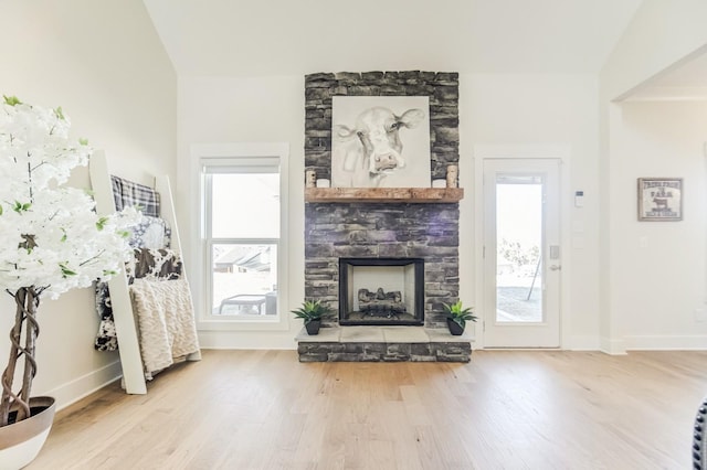 living room featuring vaulted ceiling, a stone fireplace, and hardwood / wood-style floors