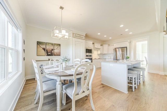 dining space featuring sink, light hardwood / wood-style floors, an inviting chandelier, and ornamental molding