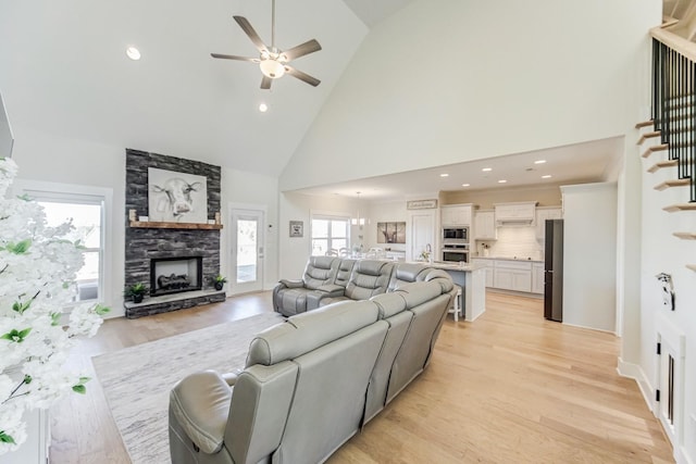 living room featuring ceiling fan, high vaulted ceiling, light hardwood / wood-style flooring, and a stone fireplace