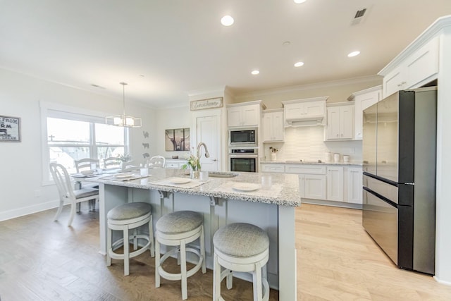 kitchen featuring appliances with stainless steel finishes, hanging light fixtures, sink, white cabinets, and an island with sink