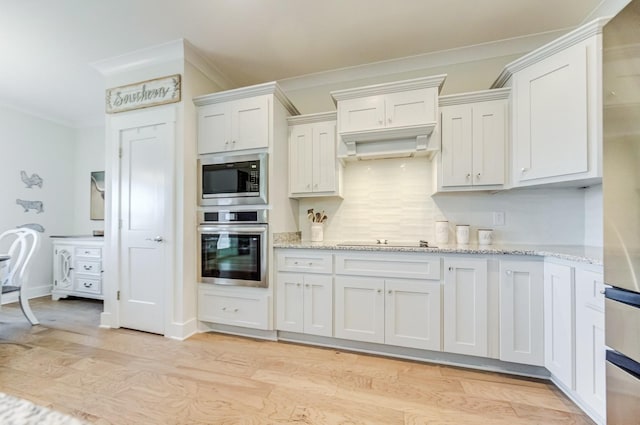 kitchen with built in microwave, white cabinetry, oven, light stone countertops, and light hardwood / wood-style floors