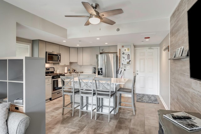 kitchen featuring gray cabinets, stainless steel appliances, decorative backsplash, a kitchen breakfast bar, and a center island