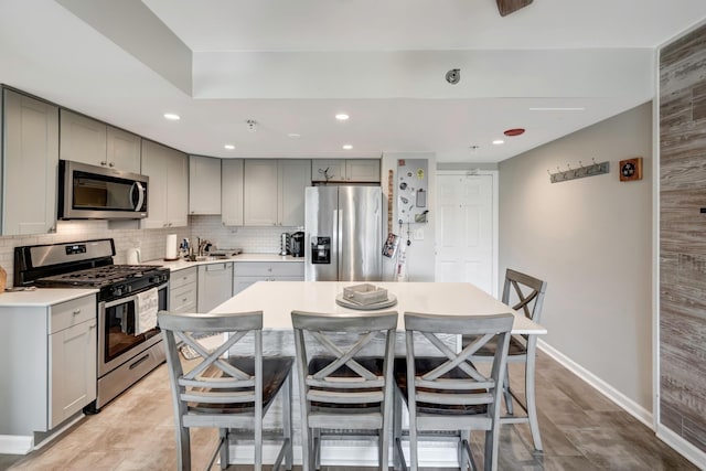 kitchen with appliances with stainless steel finishes, a kitchen island, a kitchen bar, tasteful backsplash, and gray cabinetry