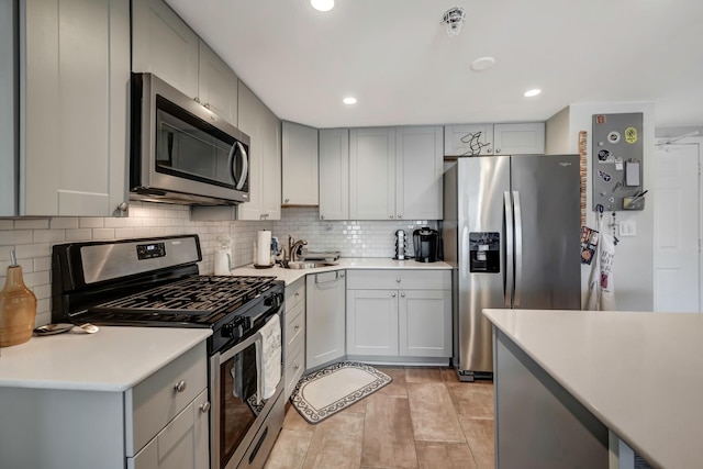 kitchen with light tile patterned floors, stainless steel appliances, gray cabinetry, decorative backsplash, and sink