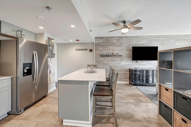 kitchen featuring wood walls, a kitchen island, stainless steel refrigerator with ice dispenser, white cabinetry, and a kitchen breakfast bar