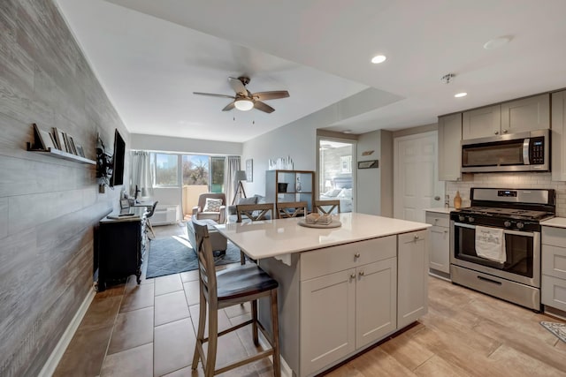 kitchen with ceiling fan, a kitchen island, a kitchen bar, gray cabinetry, and stainless steel appliances