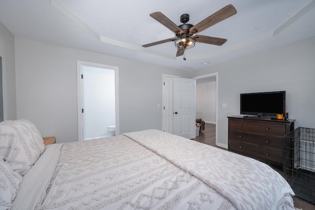 bedroom with a raised ceiling, ceiling fan, dark hardwood / wood-style floors, and ensuite bathroom