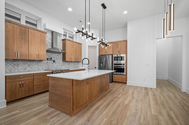 kitchen featuring pendant lighting, a kitchen island with sink, appliances with stainless steel finishes, a kitchen breakfast bar, and wall chimney exhaust hood