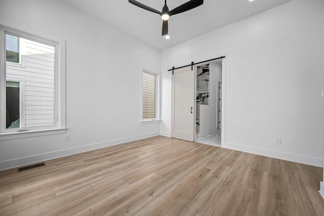 empty room featuring ceiling fan, a barn door, and light hardwood / wood-style floors