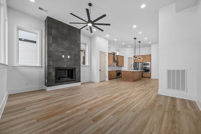 unfurnished living room with ceiling fan, a wealth of natural light, light hardwood / wood-style floors, and a fireplace