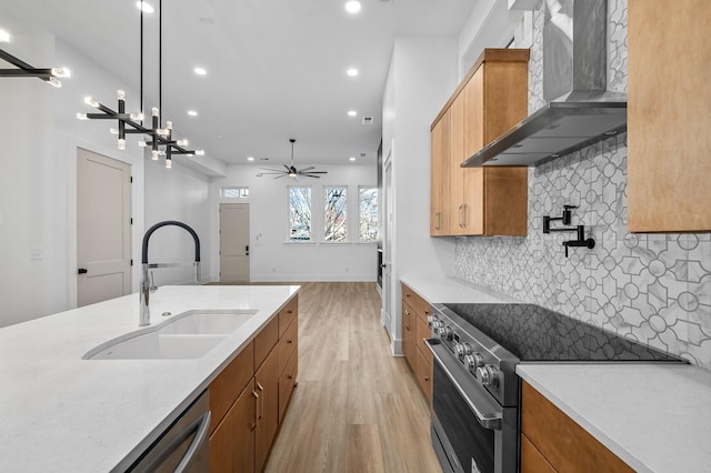 kitchen with appliances with stainless steel finishes, decorative light fixtures, light wood-type flooring, wall chimney exhaust hood, and sink