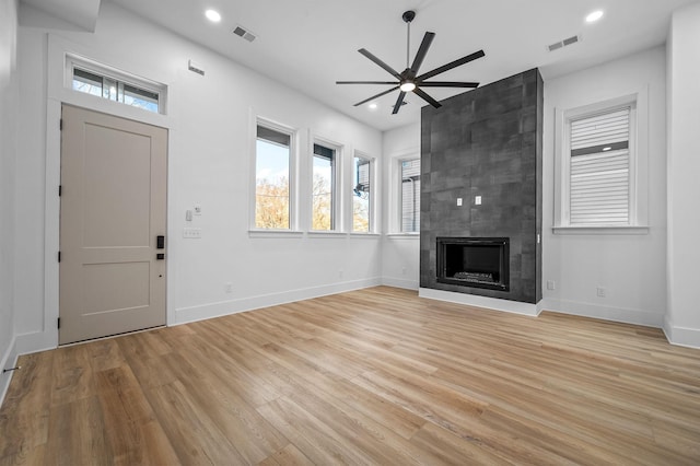 unfurnished living room featuring ceiling fan, light hardwood / wood-style flooring, and a tiled fireplace