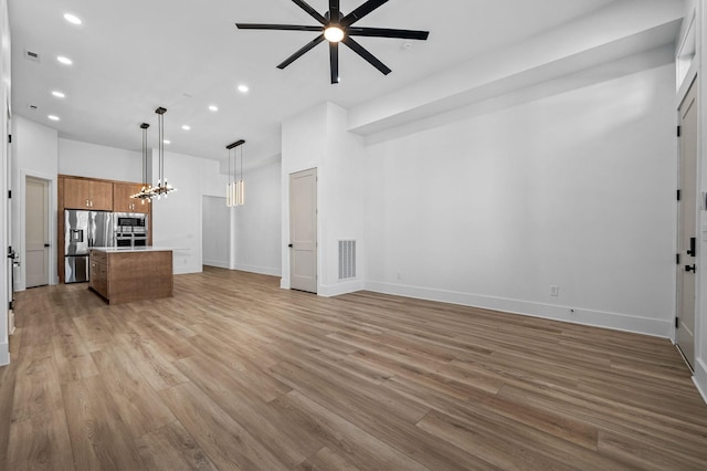 unfurnished living room featuring light wood-type flooring and ceiling fan with notable chandelier