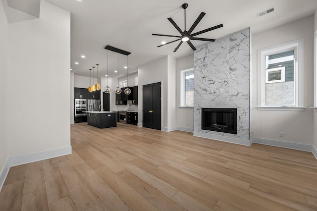 unfurnished living room featuring ceiling fan, a stone fireplace, and light hardwood / wood-style flooring