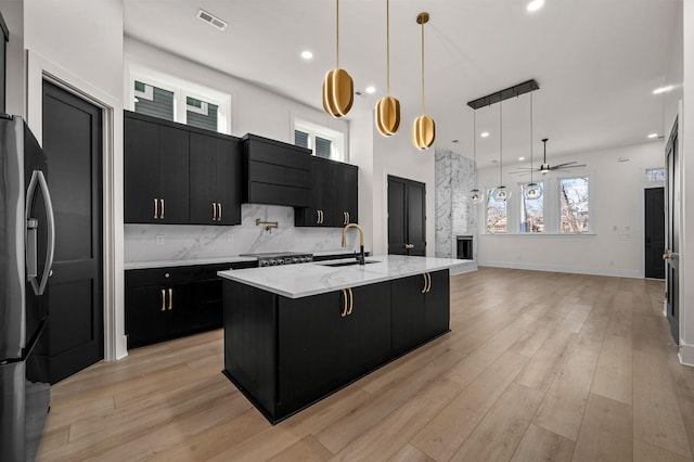 kitchen featuring a large island, a breakfast bar area, black fridge with ice dispenser, hanging light fixtures, and sink