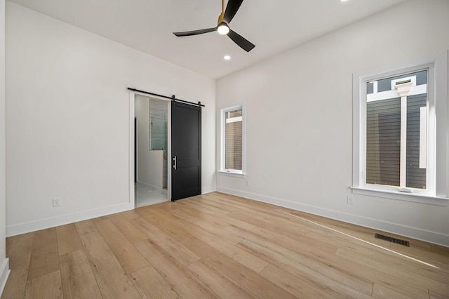 unfurnished bedroom featuring ceiling fan, multiple windows, a barn door, and light wood-type flooring