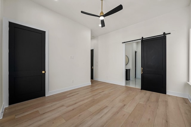 unfurnished bedroom featuring ceiling fan, a barn door, and light wood-type flooring