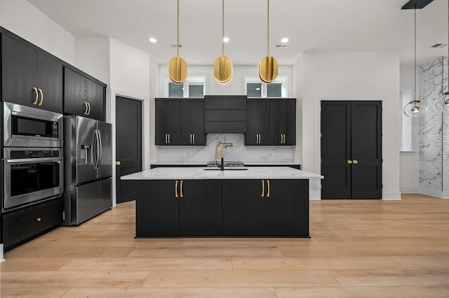 kitchen featuring appliances with stainless steel finishes, light hardwood / wood-style flooring, a center island with sink, and hanging light fixtures