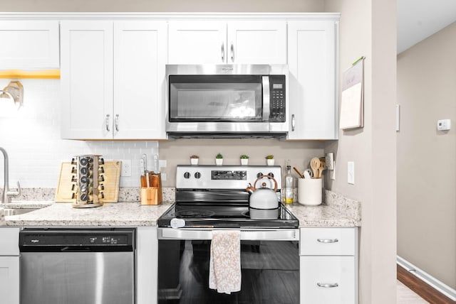 kitchen featuring light stone countertops, white cabinetry, stainless steel appliances, decorative backsplash, and sink