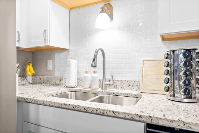 kitchen featuring white cabinetry, black dishwasher, sink, backsplash, and light stone counters