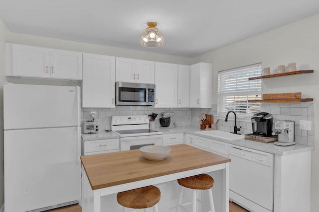 kitchen featuring a kitchen island, sink, white appliances, white cabinetry, and a kitchen breakfast bar