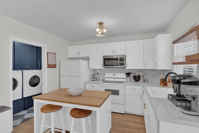 kitchen with washer and dryer, a center island, sink, white appliances, and white cabinetry