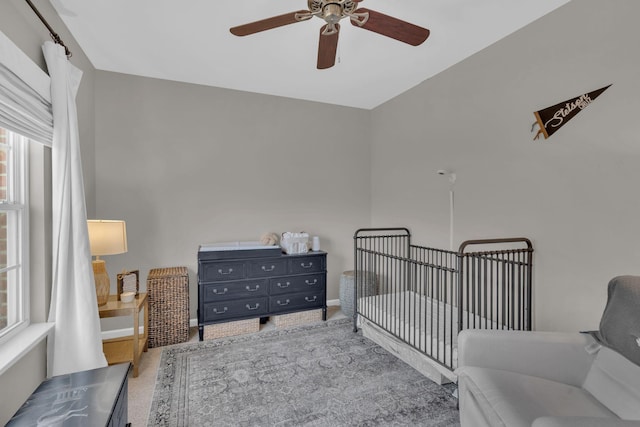 carpeted bedroom featuring ceiling fan and a crib