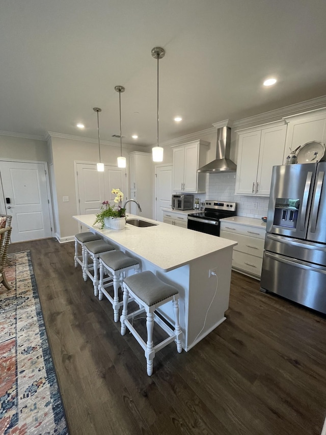 kitchen featuring wall chimney range hood, a kitchen island with sink, appliances with stainless steel finishes, a kitchen breakfast bar, and white cabinets