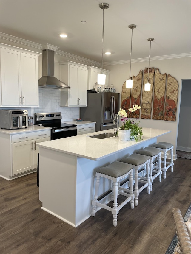 kitchen with decorative light fixtures, appliances with stainless steel finishes, wall chimney range hood, and a center island with sink