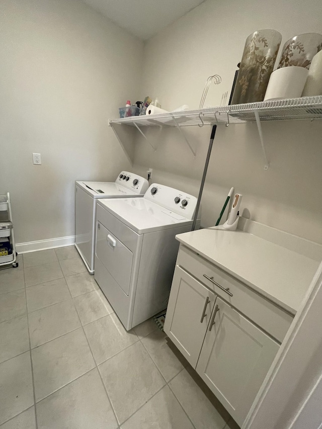 clothes washing area with washing machine and dryer, light tile patterned flooring, and cabinets