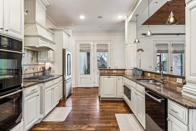 kitchen featuring white cabinets, decorative light fixtures, stainless steel appliances, dark stone countertops, and sink