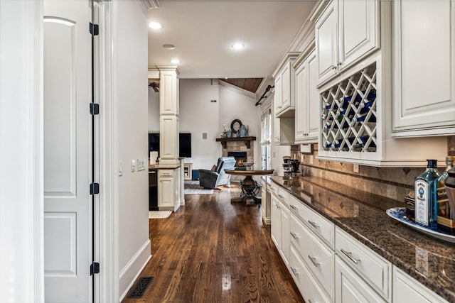 kitchen featuring dark stone counters, dark hardwood / wood-style flooring, white cabinetry, and decorative columns