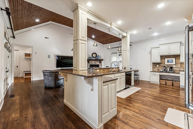 kitchen with a kitchen island with sink, a kitchen breakfast bar, hanging light fixtures, dark stone counters, and sink