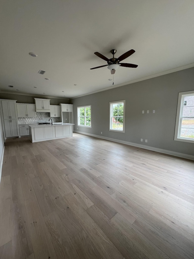 unfurnished living room with light hardwood / wood-style floors, sink, ornamental molding, and ceiling fan