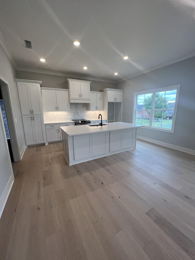 kitchen with a center island with sink, backsplash, light wood-type flooring, white cabinets, and sink