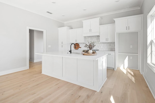 kitchen with sink, white cabinetry, a kitchen island with sink, light hardwood / wood-style floors, and backsplash