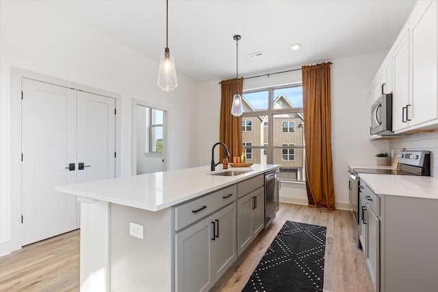 kitchen featuring gray cabinets, pendant lighting, sink, an island with sink, and stainless steel appliances