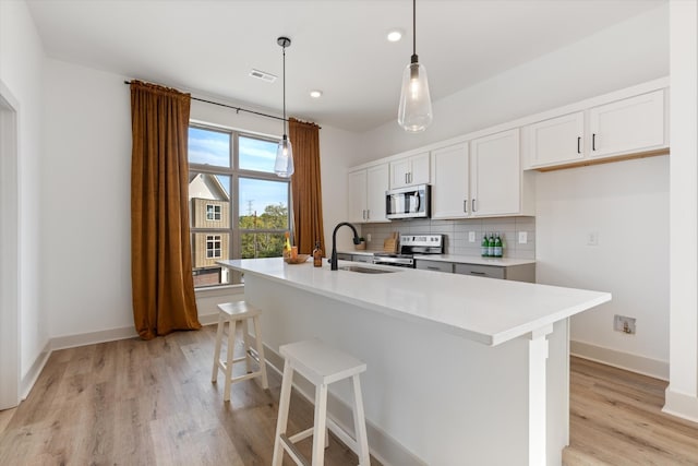 kitchen with appliances with stainless steel finishes, white cabinetry, sink, hanging light fixtures, and a kitchen island with sink