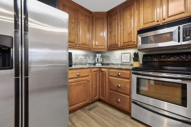 kitchen with stainless steel appliances, dark stone countertops, and light hardwood / wood-style floors